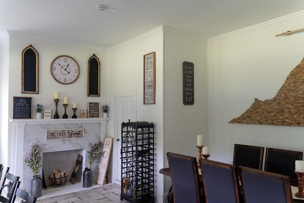 Una habitación con chimenea, un reloj y diversas decoraciones en la pared, incluyendo frases enmarcadas y una pizarra.