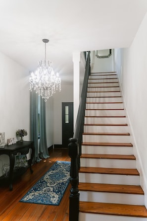 A staircase with wooden steps and a black handrail, leading to a landing with a chandelier and a table with a rug. - Charming 5-bedroom farmhouse with AC in peaceful Hustle (Hustle)
