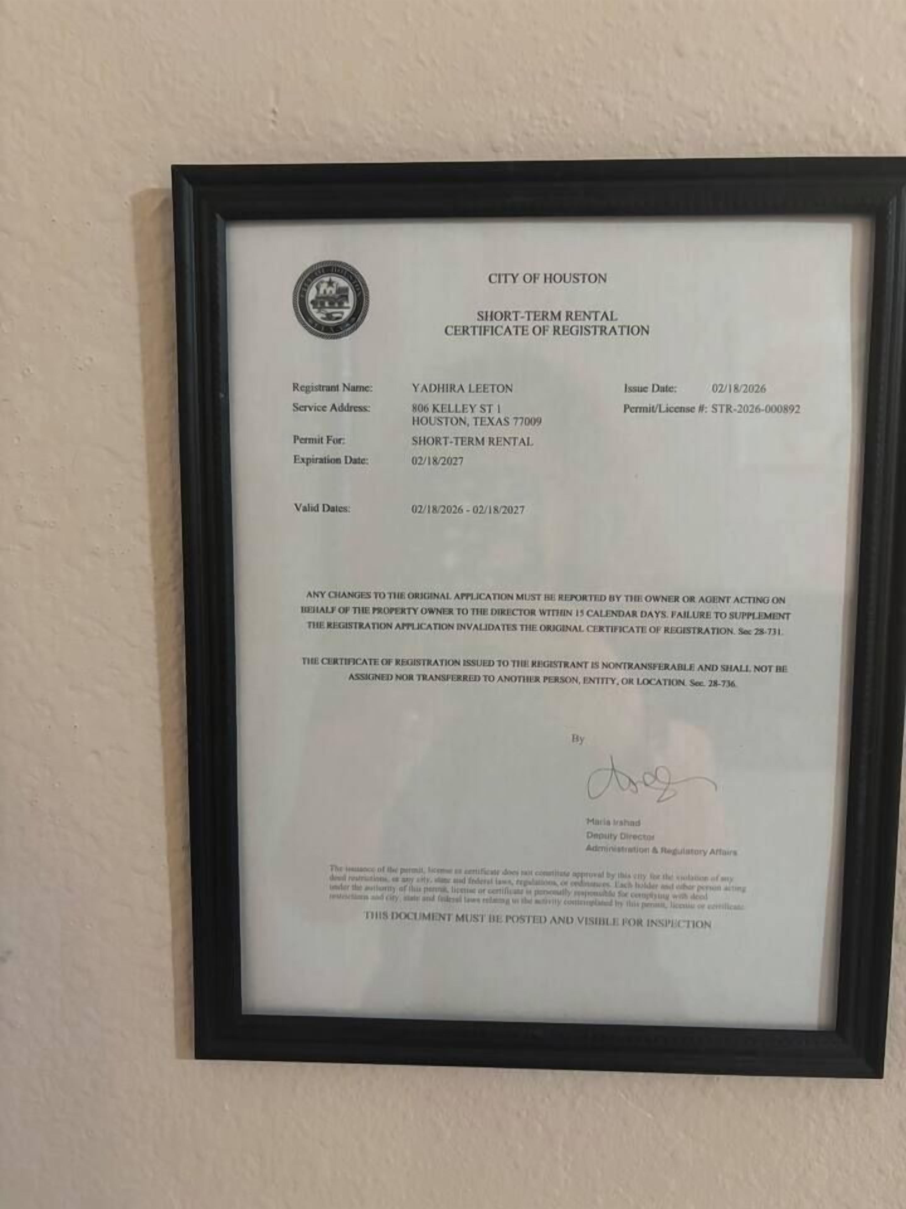 A framed short-term rental certificate of registration for Yadhira Leeton, dated 02/18/2026, with a permit/license number STR-2026-000892.