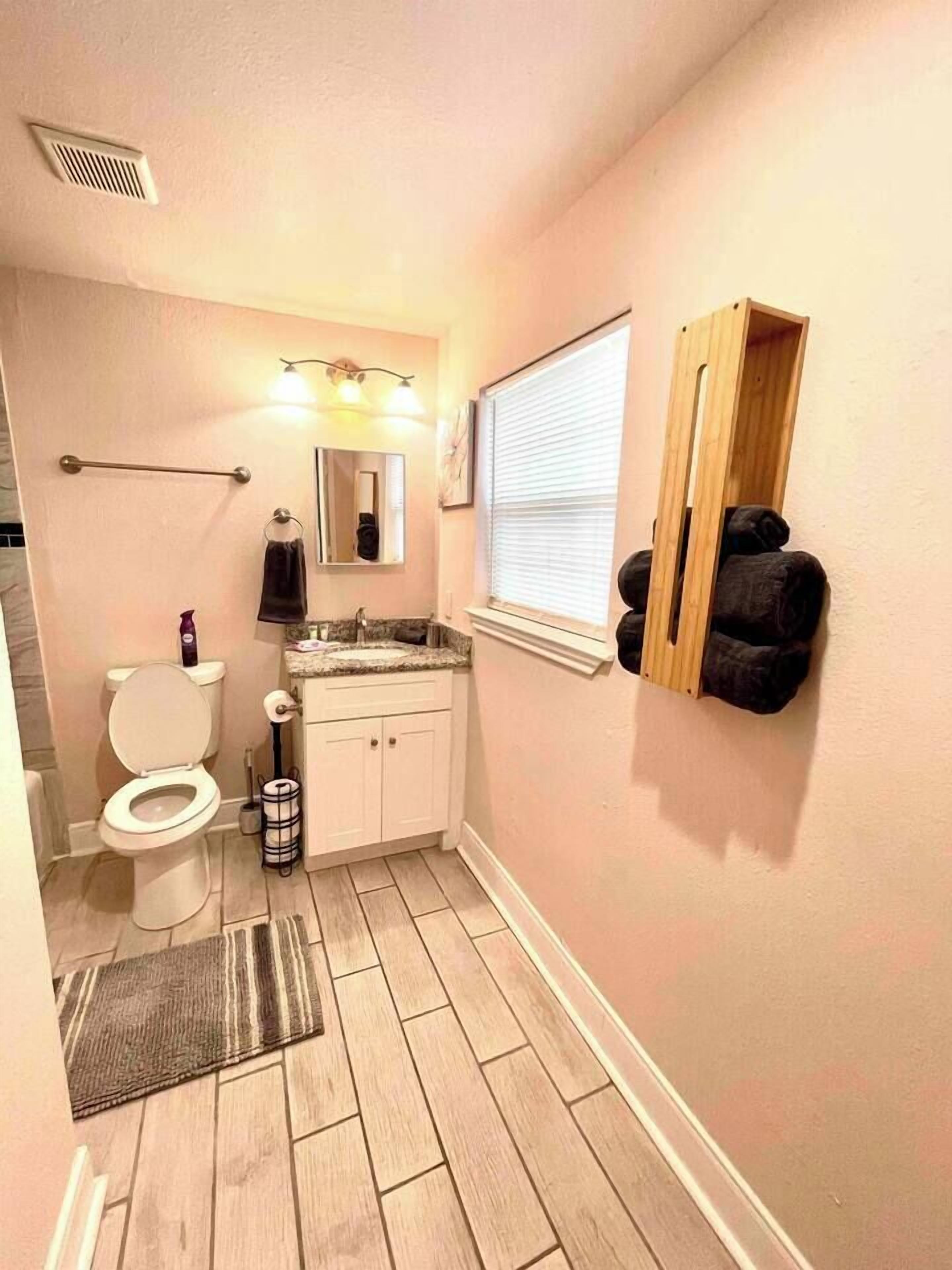 A small bathroom with a toilet, sink, vanity, mirror, towel rack, and a window.
