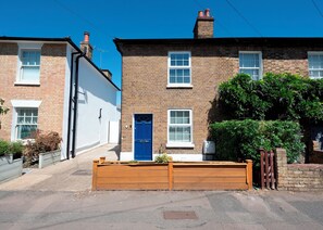 A residential street with two brick houses, one with a blue door, and a wooden fence in the foreground. - Charming Cottage 15 minutes to central London - Pass the Keys (Surbiton)