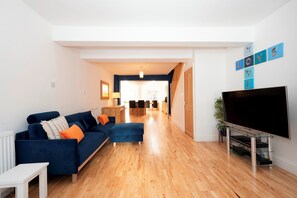 A modern living room with a sofa, ottoman, and a flat-screen TV. - Charming Cottage 15 minutes to central London - Pass the Keys (Surbiton)