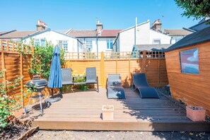 Une terrasse en bois avec des chaises longues et un barbecue.