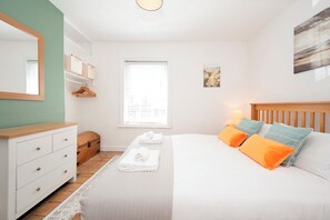 Une chambre à coucher avec un lit, une commode, un panier suspendu, une fenêtre et un tableau au mur.