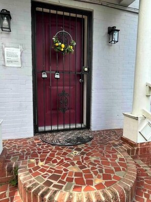 A red door with a decorative wreath, a black metal gate, and a tiled entrance area. - Cozy Retreat w/Coffee Bar & Private Entry (Houston)