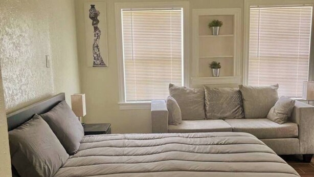 A bedroom with a large bed, a sofa, and two windows with blinds. - Cozy Retreat w/Coffee Bar & Private Entry (Houston)