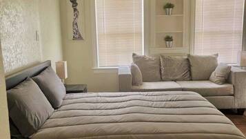 Een slaapkamer met een groot bed, een sofa en twee ramen met jaloezieën.
