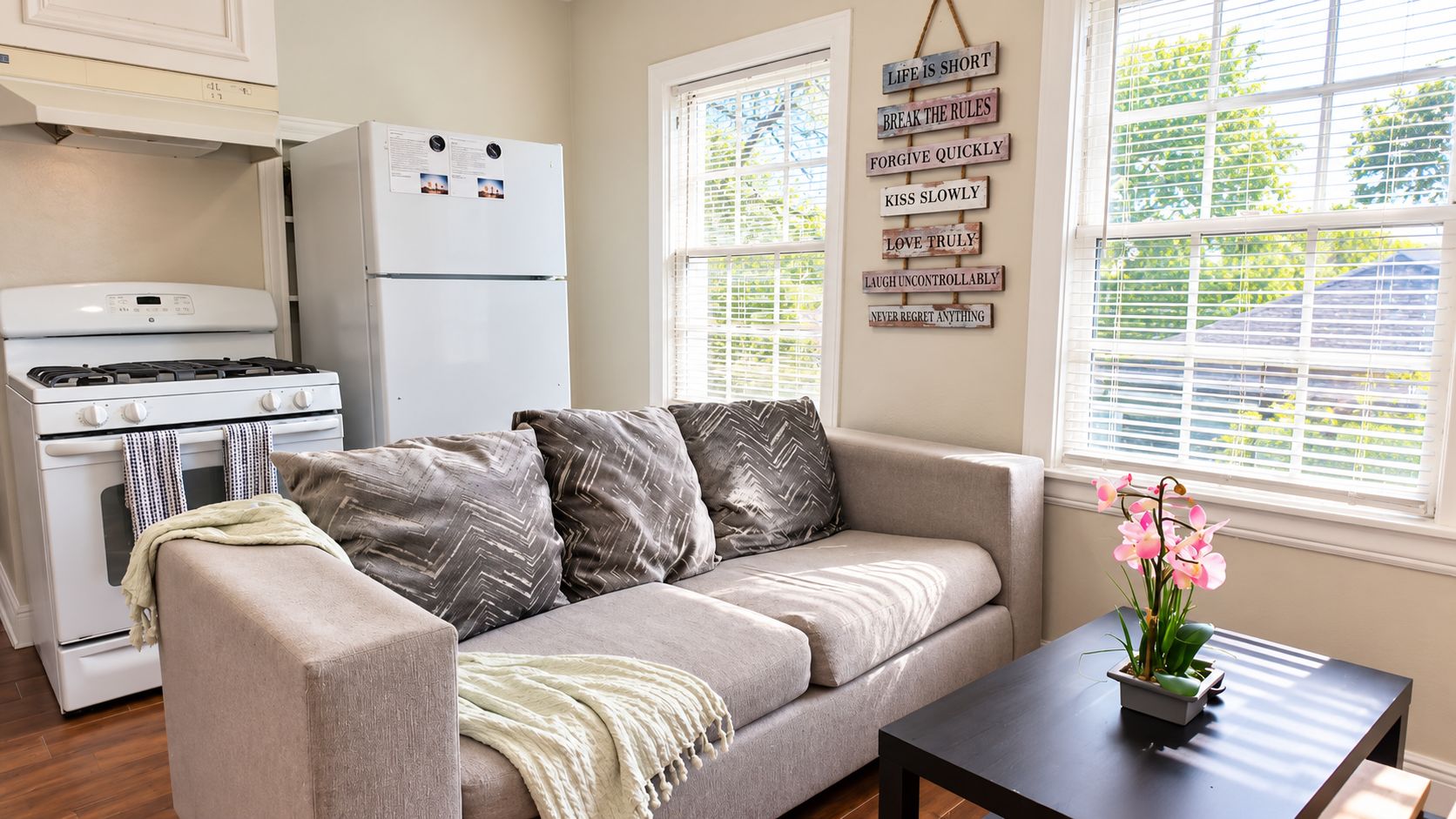 Una sala de estar acogedora con un sofá, una pequeña mesa con una planta y una zona de cocina con estufa y refrigerador.