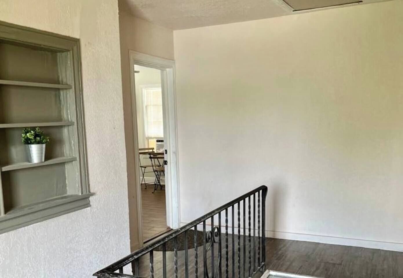 Una habitación con una escalera, una ventana con una planta y una puerta que da a otra habitación.