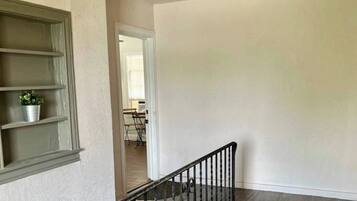 Una habitación con una escalera, una ventana con una planta y una puerta que da a otra habitación.