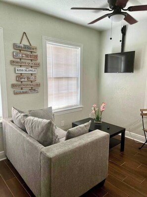 A living room with a grey sofa, a black coffee table, and a wall-mounted TV. - Cozy Retreat w/Coffee Bar & Private Entry (Houston)