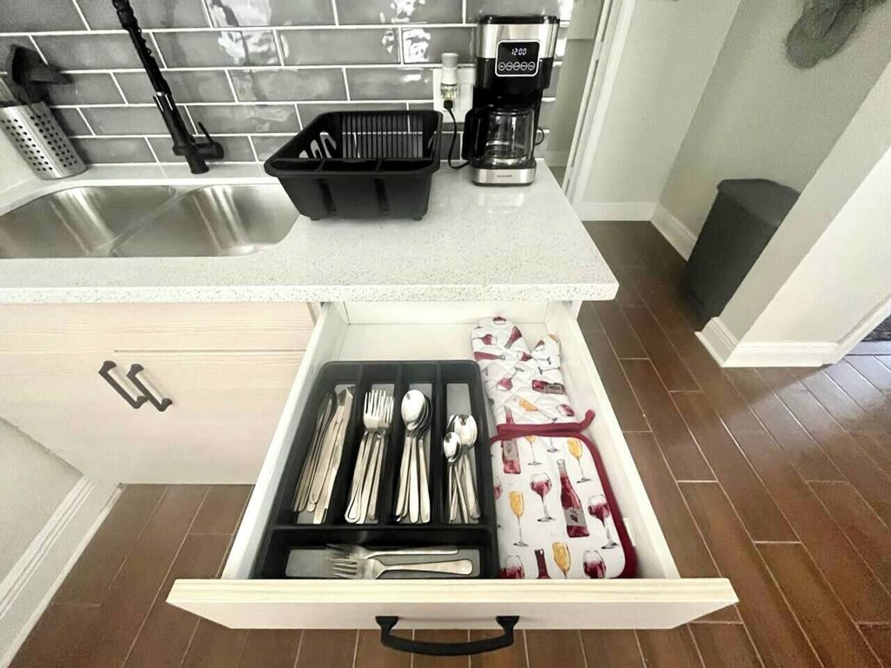 Een keuken met een roestvrijstalen spoelbak, een koffiezetapparaat en een ladeorganizer met keukengerei.