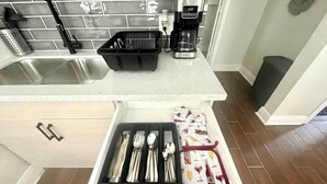 A kitchen with a stainless steel sink, a coffee maker, and a drawer organizer with utensils. - Cozy Retreat w/Coffee Bar & Private Entry (Houston)