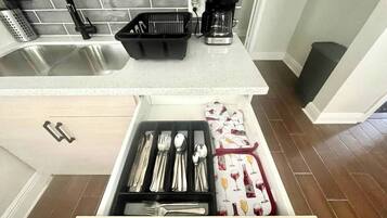 Een keuken met een roestvrijstalen spoelbak, een koffiezetapparaat en een ladeorganizer met keukengerei.