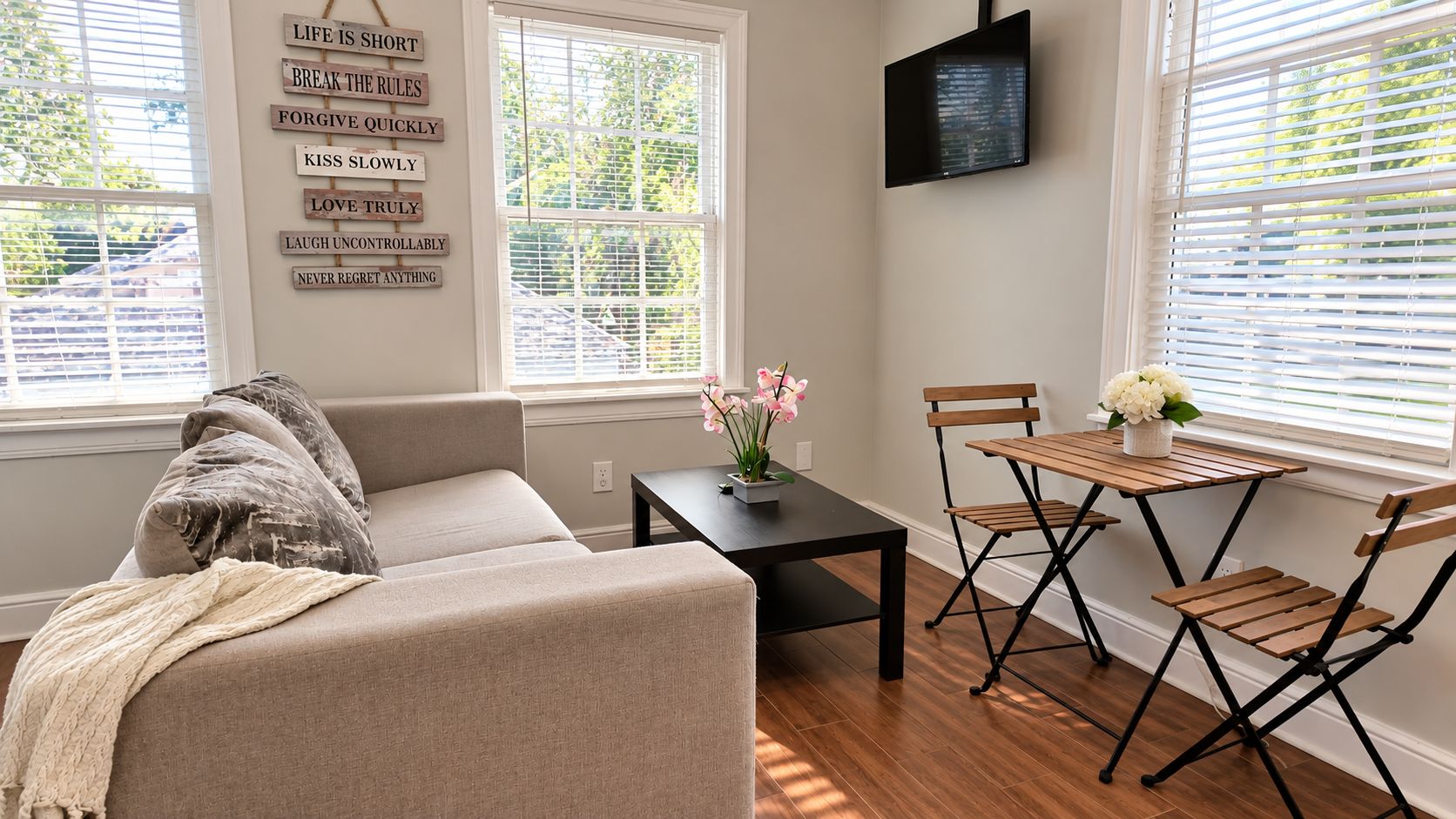 A living room with a sofa, a small table with a vase of flowers, and a TV mounted on the wall.