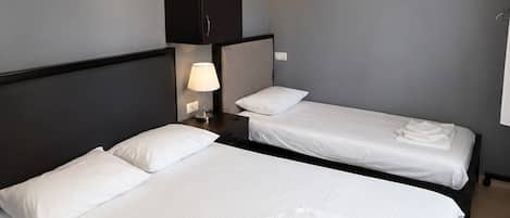 A hotel room with two single beds, a dark wardrobe, a wall-mounted clock, and an air conditioning unit.