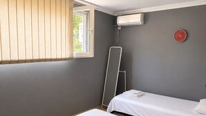 A hotel room with two beds, a window with blinds, an air conditioning unit, and a red wall clock. - Lovely private house on the Shekvetili coast (Shekvetili)