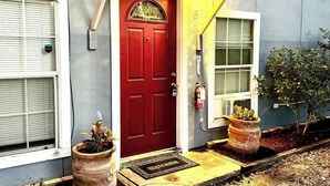 Une porte rouge avec un paillasson, une petite plante en pot et un extincteur fixé au mur.