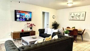Un salon avec un canapé noir, une table basse, un téléviseur et un ventilateur de plafond.
