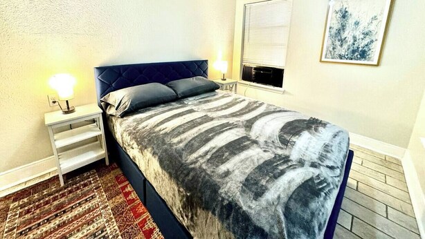Une chambre à coucher avec un lit, des lampes de chevet, un ventilateur de plafond, une fenêtre avec des stores et un tableau encadré au mur.