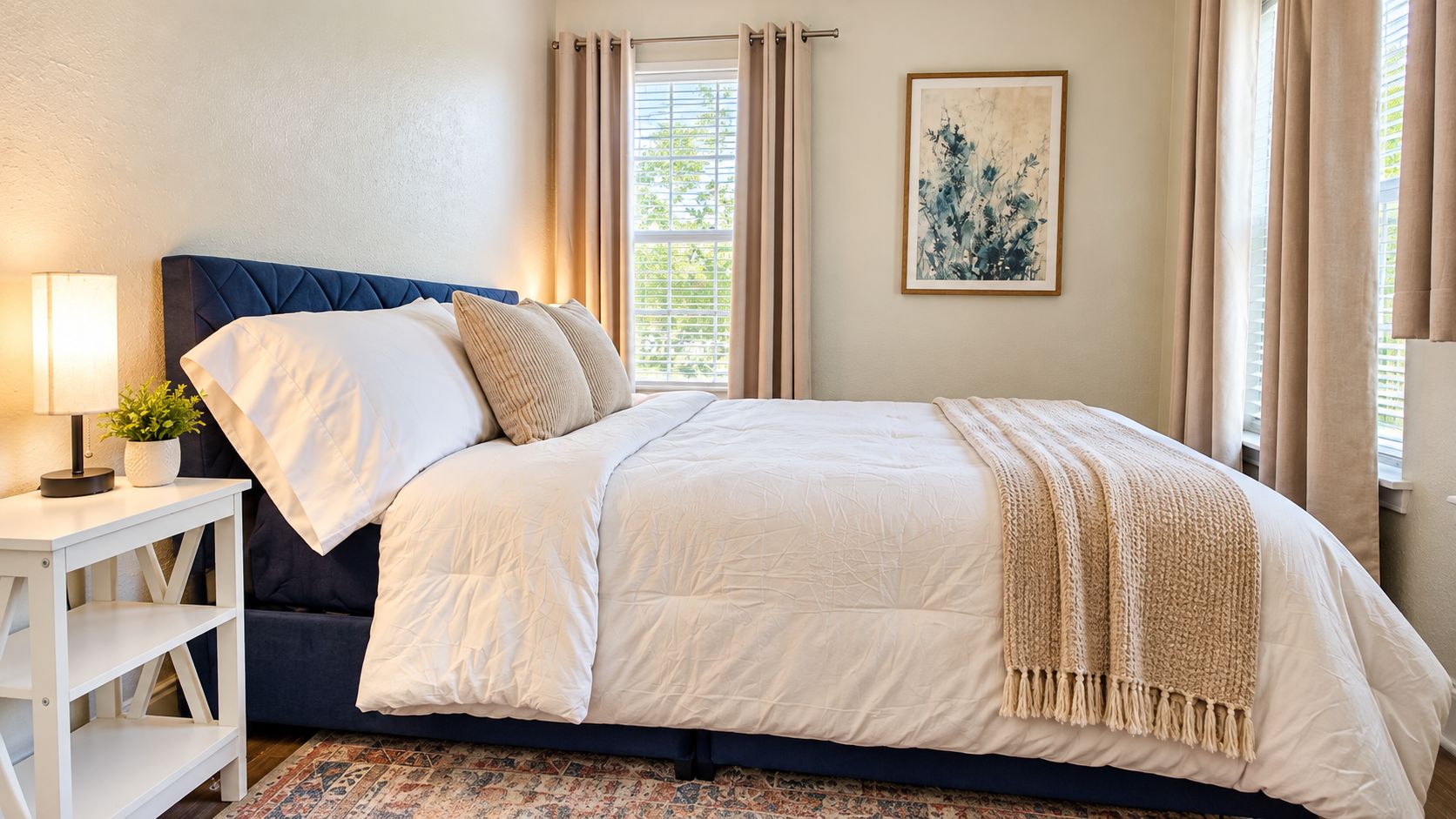 Un dormitorio con cama, mesita de noche, lámpara y ventana con cortinas.