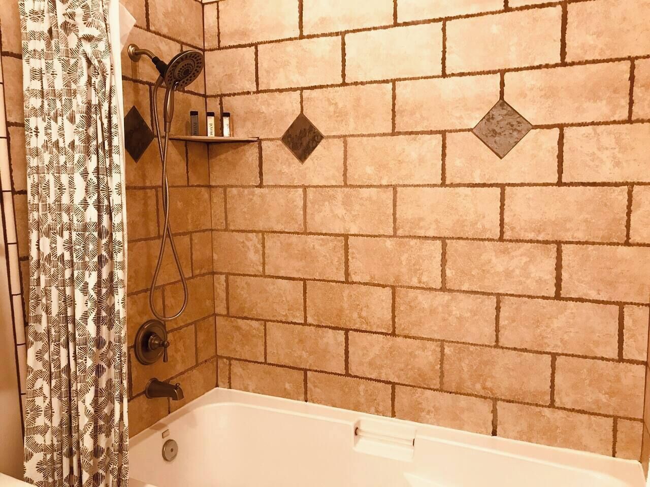 A bathroom with a bathtub, shower, and patterned curtain.