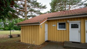 A yellow building with a red-tiled roof, a white door, and a small window with a curtain. - Modern Eingerichteter Doppelbungalow mit Garten in Mirow (Mirow)