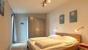 A bedroom with two beds, a wooden headboard, a nightstand, and a wall-mounted lamp. - Modern Eingerichteter Doppelbungalow mit Garten in Mirow (Mirow)