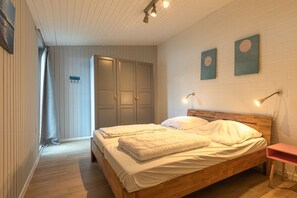 A bedroom with two beds, a wooden headboard, a nightstand, and a wall-mounted lamp. - Modern Eingerichteter Doppelbungalow mit Garten in Mirow (Mirow)