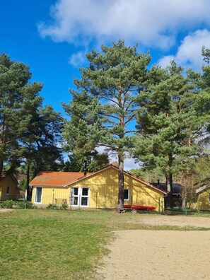 A yellow building with a red roof, surrounded by trees and a grassy area. - Modern Eingerichteter Doppelbungalow mit Garten in Mirow (Mirow)
