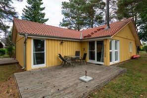 A yellow building with a red-tiled roof, large windows, and a wooden deck with outdoor furniture. - Modern Eingerichteter Doppelbungalow mit Garten in Mirow (Mirow)