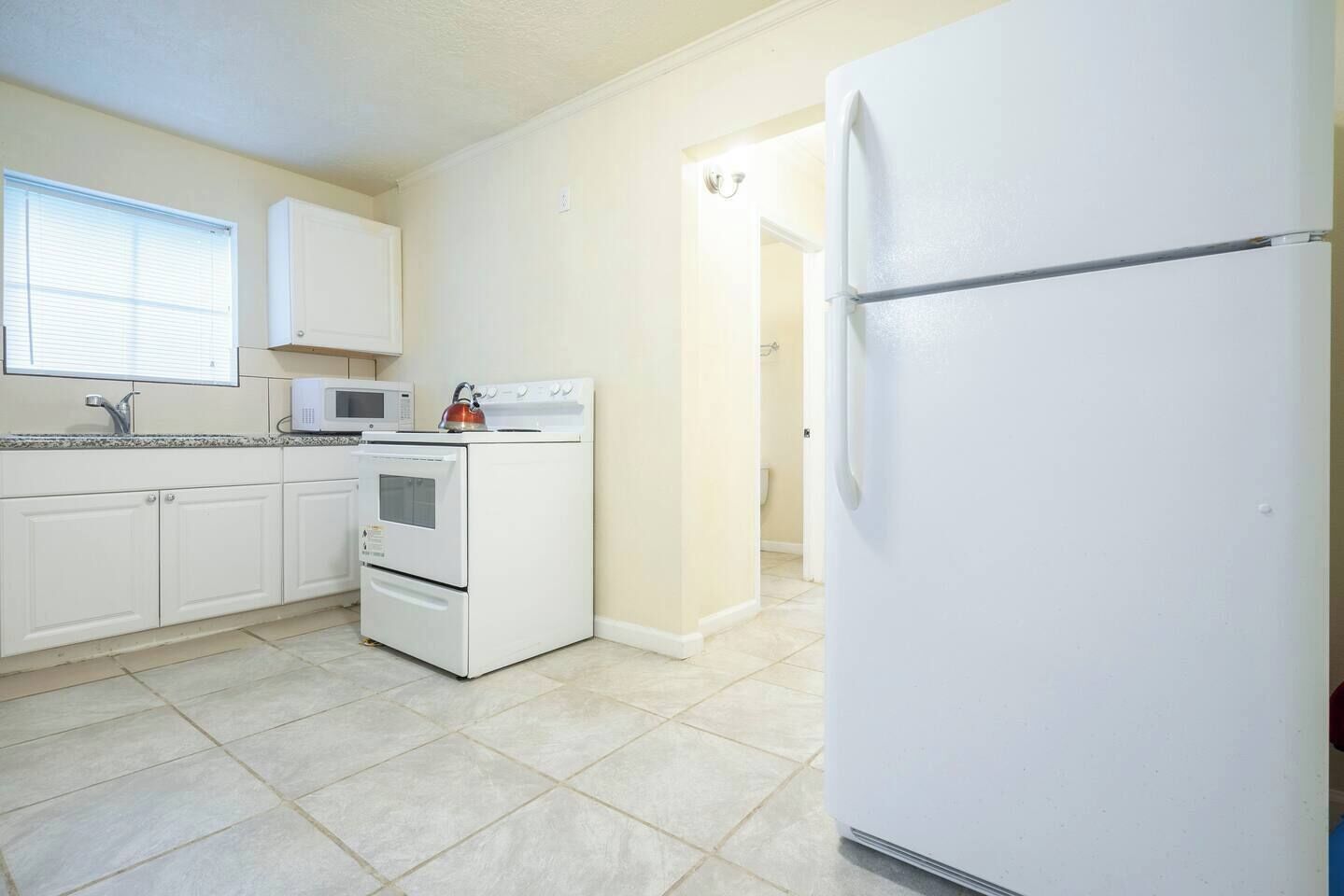 A kitchen with white cabinets, a stove, a microwave, and a refrigerator.