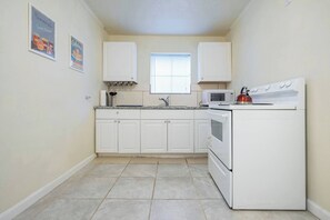 A compact kitchen with white cabinets, a microwave, a stove, and a window with blinds. - Pet-Friendly Houston Apartment w\ Backyard (Houston)