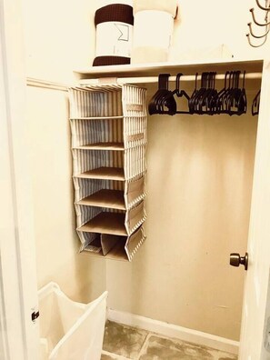 A closet with hanging clothes, a storage unit, and a white trash bin. - Pet-Friendly Houston Apartment w\ Backyard (Houston)