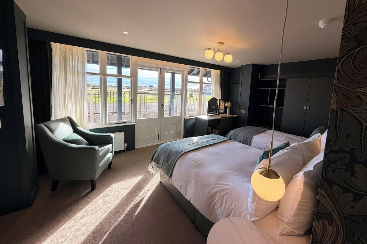 Habitación de hotel con una cama grande, un escritorio, una silla y vistas al exterior.