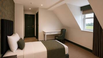 A bedroom with a bed, a desk, and a chair. There is a window with curtains.