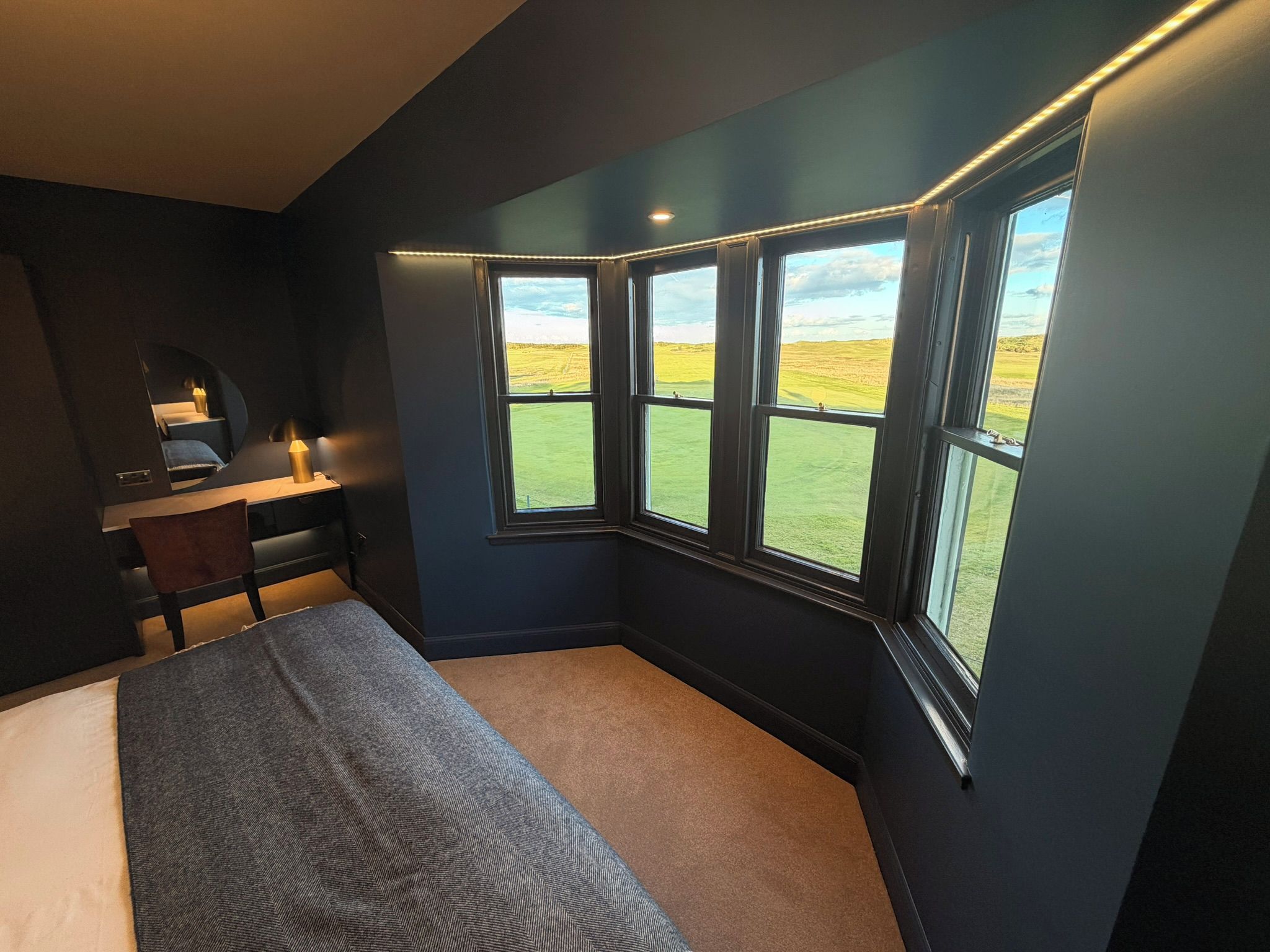 A bedroom with a bed, a desk, and a window with a view of a field.