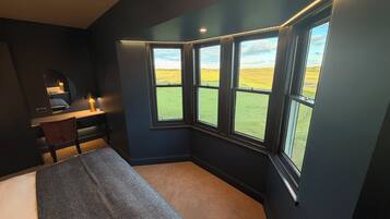A bedroom with a bed, a desk, and a window with a view of a field.