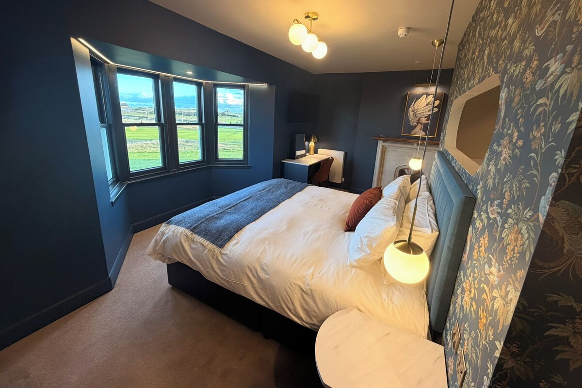 Un dormitorio con una cama grande, un escritorio y vistas al exterior a través de una ventana.