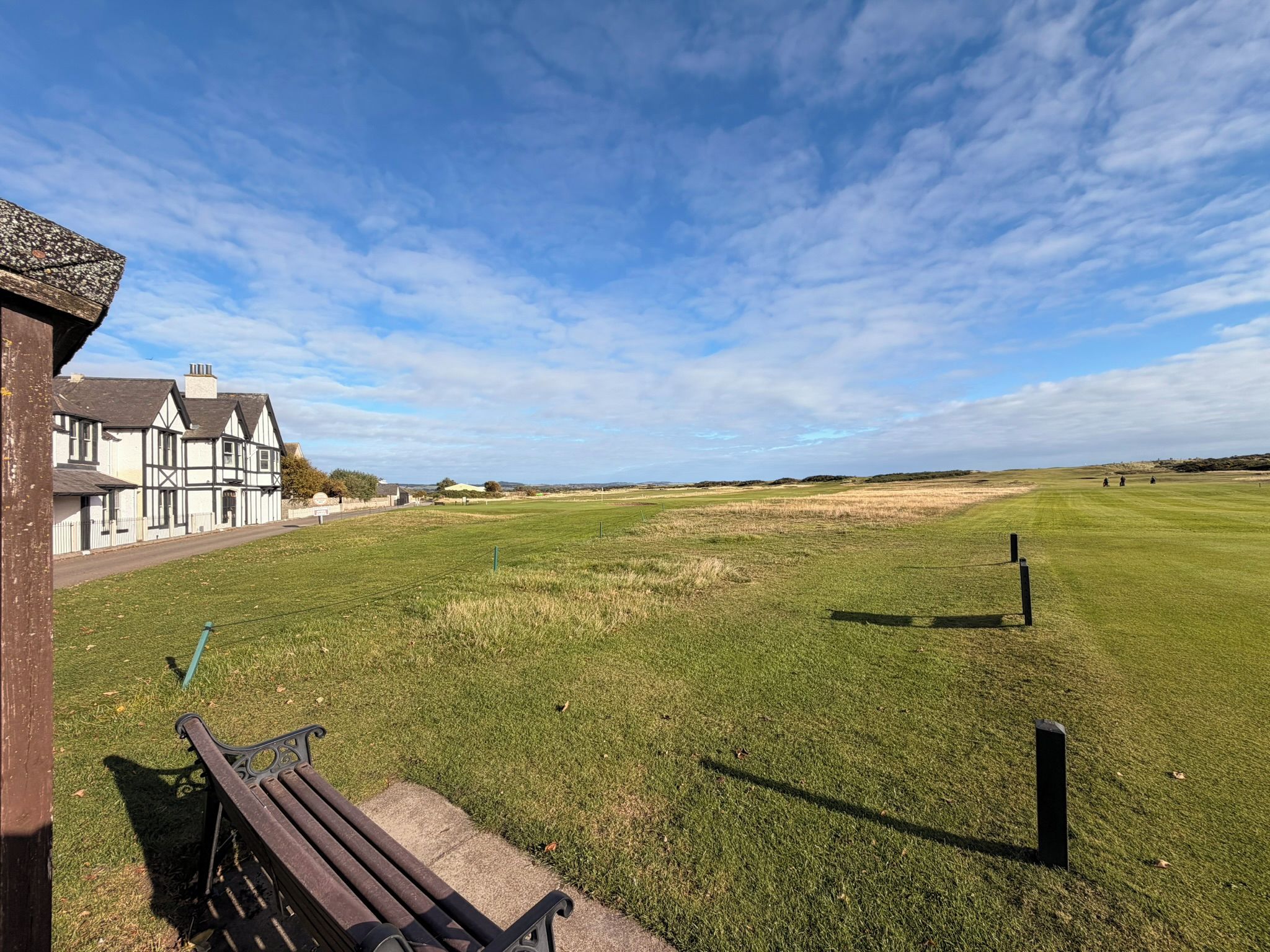A grassy field with a bench and a building with white walls and dark roofs.