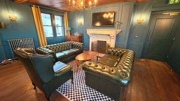 A room with a checkered floor, a fireplace, a television mounted above it, and a chandelier.