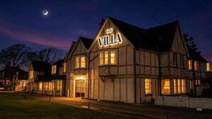 A traditional building with a sign reading 'The Villa' at night, featuring a prominent entrance and multiple windows.