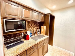 A kitchen with a microwave, sink, and wooden cabinets. - Bellaire Home Stay w/Pool & Workspace (Houston)