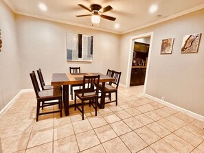 A dining area with a rectangular table and six chairs, a ceiling fan, and a kitchen visible through an open doorway. - Bellaire Home Stay w/Pool & Workspace (Houston)