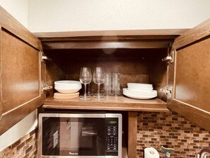 A kitchen with a microwave and a cabinet containing stacked plates and wine glasses. - Bellaire Home Stay w/Pool & Workspace (Houston)
