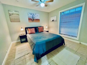 A bedroom with a bed, two bedside tables, a ceiling fan, and a large window with blinds. - Bellaire Home Stay w/Pool & Workspace (Houston)