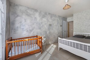 A bedroom with a crib, a bed, and a hanging light fixture. - Bournezeau Holiday Cottage in the Countryside, Near Coast and Attractions (Bournezeau)