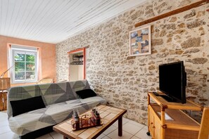 A cozy living room with a stone wall, a sofa, a television, and a small table with glasses. - Bournezeau Holiday Cottage in the Countryside, Near Coast and Attractions (Bournezeau)