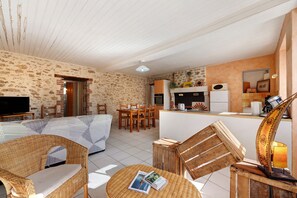 Ein gemütliches Wohnzimmer mit einer Couch, Sesseln, einem Fernseher und einem Essbereich mit Tisch und Stühlen.