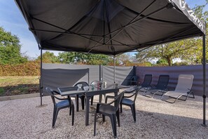 An outdoor patio with a table and chairs, a large umbrella, and a seating area with lounge chairs. - Bournezeau Holiday Cottage in the Countryside, Near Coast and Attractions (Bournezeau)